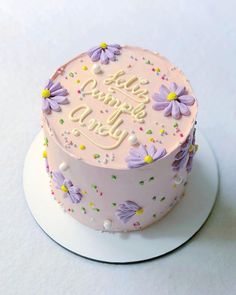 a pink birthday cake decorated with purple flowers and sprinkles on a white plate