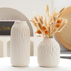 two white vases sitting on top of a table next to each other with flowers in them