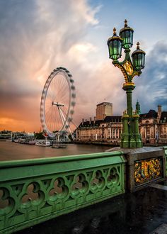 a ferris wheel sitting next to a river under a cloudy sky with buildings in the background