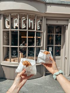 two hands holding up some food in front of a storefront with the words creme written on it