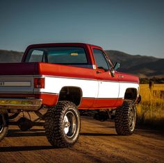 a red and white truck parked on top of a dirt road next to a field