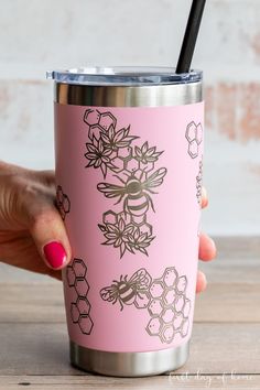 a woman's hand holding a pink tumbler cup with bees and honeycombs on it