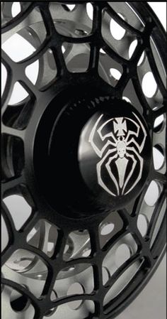 an image of a black and silver fly fishing reel with spider logo on the side