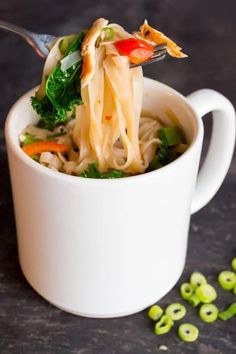 a spoon full of noodles and vegetables being lifted from a white cup with broccoli sprouts