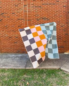 two quilts sitting on the ground next to a brick wall in front of a building