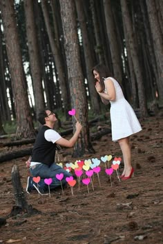 a man kneeling down next to a woman in front of a forest filled with trees