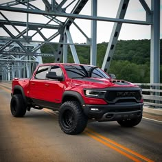 a red truck is driving down the road by some metal bridge tracks and trees in the background