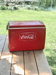 a red cooler sitting on top of a wooden table in front of a green field