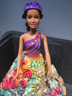 a barbie doll dressed in a colorful dress and tiara with flowers on the skirt