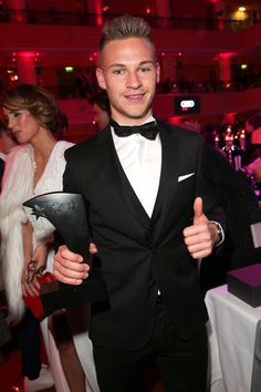 a man in a tuxedo is holding an award and giving the thumbs up