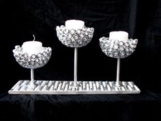 three white candles sitting on top of a metal tray with silver balls and beads around them