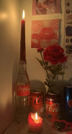 a candle and some coca - cola cans are sitting on a table next to a vase with roses