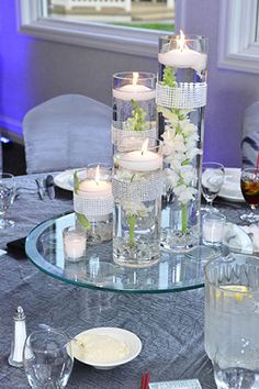 a table topped with lots of candles and vases filled with flowers on top of it