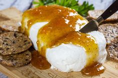 a wooden cutting board topped with cheese covered in gravy next to crackers