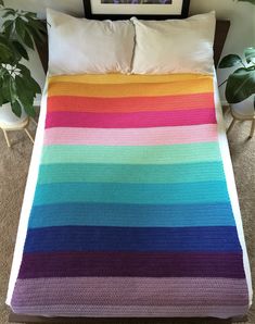 a bed with a colorful blanket on top of it next to a potted plant