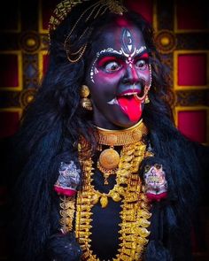 a woman in black and gold costume with her tongue sticking out to the side while wearing an elaborate headdress