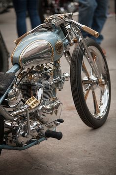 a silver motorcycle parked on top of a cement floor next to other motorcycles and people