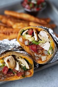 two burritos are wrapped in foil with meat and veggies