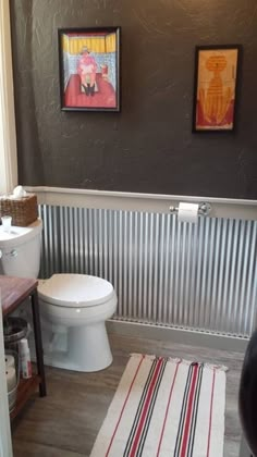 a white toilet sitting in a bathroom next to a wooden table and wall with pictures on it