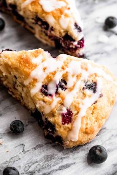 two blueberry scones with icing sitting on a marble surface