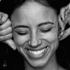 a black and white photo of a woman smiling with her hands on her head,