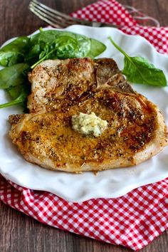 a white plate topped with meat and spinach on top of a red checkered table cloth