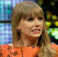 a close up of a person with long hair and wearing an orange dress on the set of tv