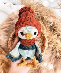 a hand holding a small crocheted stuffed bird in a red hat and scarf