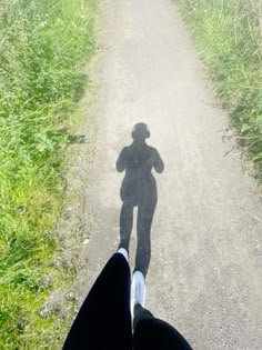 a person standing in the middle of a dirt road with their shadow on the ground