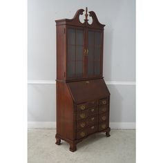 an antique wooden desk and hutch with glass doors on the top, against a white wall