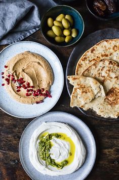 three plates with pita bread, hummus and olives