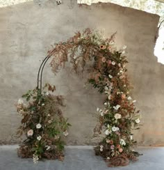 an arch made out of branches and flowers on the side of a building with concrete walls