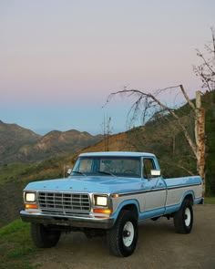 an old pick up truck parked on the side of a road in front of mountains