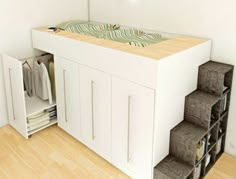 a room with a bed and some drawers on the floor next to a shelf filled with clothes