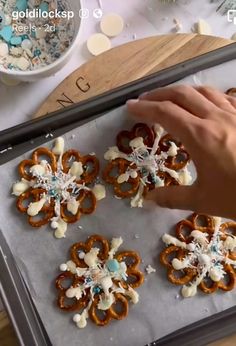 someone is decorating pretzels with white and blue decorations on a baking sheet