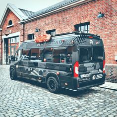 a black bus parked in front of a brick building on a cobblestone street