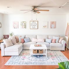 a living room with white couches and lots of pillows on top of the rug