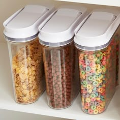 three plastic containers filled with cereal and cereal flakes on top of a white shelf