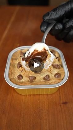 a person in black gloves spooning ice cream into a cookie