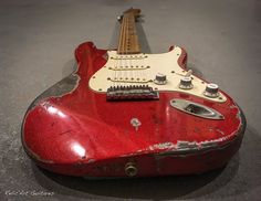 an old red guitar sitting on the ground