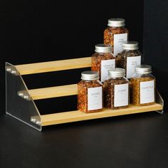 six jars with labels on them sitting on a wooden shelf in front of a black background