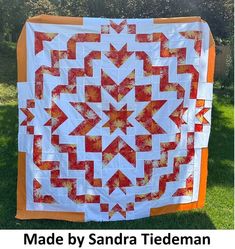 an orange and white quilt hanging on the side of a fence with text overlay that reads made by sandra tideman