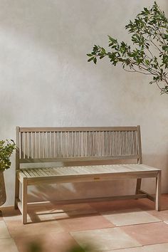 a wooden bench sitting next to a potted plant on a tiled floor in front of a white wall