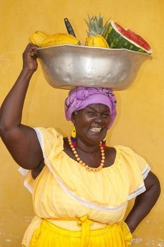 a woman with a large bowl on her head and fruit in the middle of her head