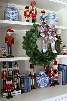 a christmas wreath on top of a book shelf next to figurines and books