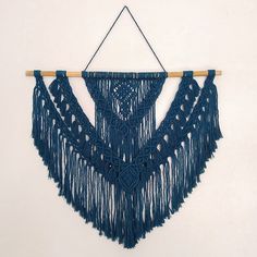 a blue crocheted wall hanging on a white wall next to a wooden stick