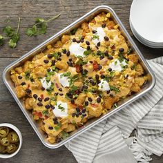 a casserole dish with black beans, corn and sour cream on top next to some olives