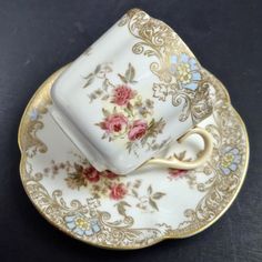 an antique tea cup and saucer with pink roses on the side, sitting on a black surface