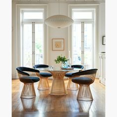 an oval glass table with four chairs and a vase on the top is surrounded by windows