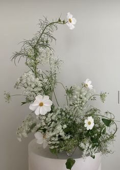 white flowers and greenery are arranged in a round vase on top of a table